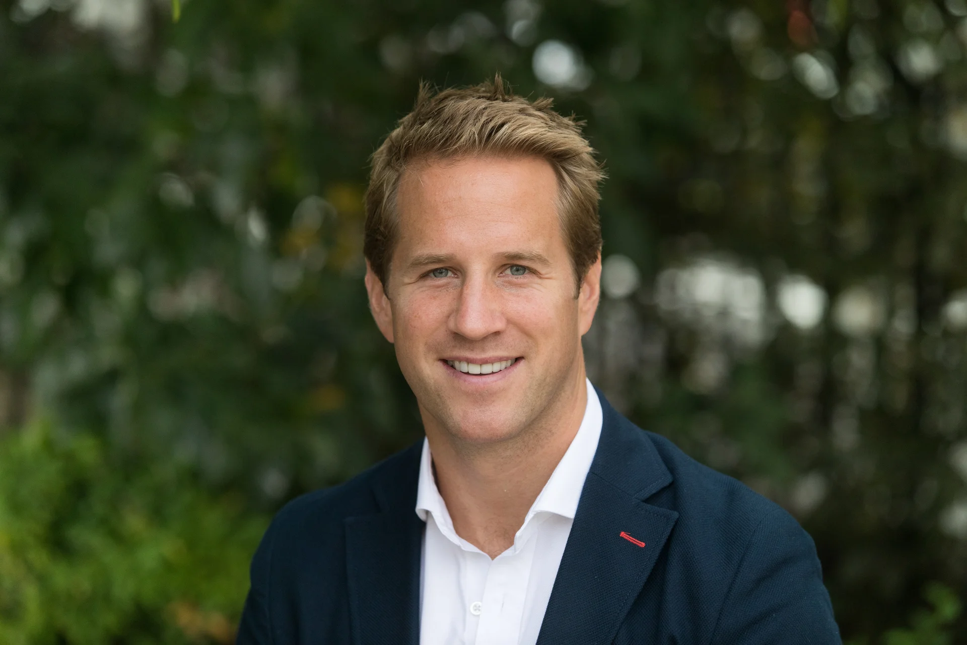 Professional headshot of Harry Foster, Leasing Director. He is smiling and wearing a blazer, set against a natural, blurred green background.