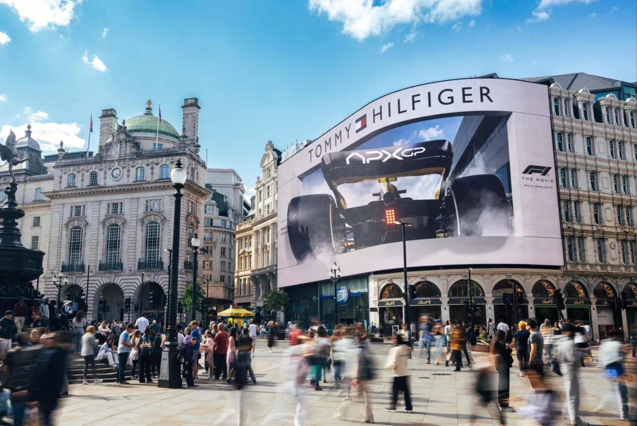 The iconic **Piccadilly Lights** digital billboard in London displaying a **Tommy Hilfiger** advertisement featuring a race car, with crowds in **Piccadilly Circus** below.