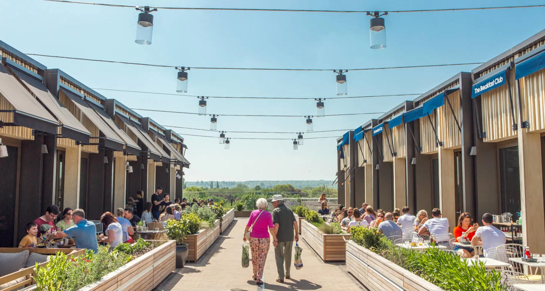 Outdoor dining area at The Breakfast Club with people at tables, planters, and string lights.