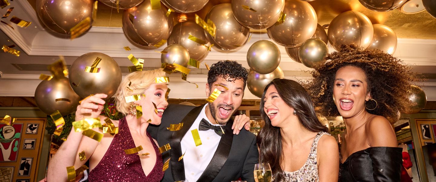 People in black tie dress holding glasses of champagne surrounded by gold balloons