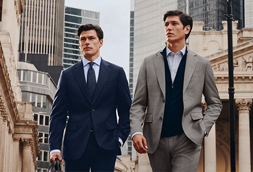 Two men wearing suits walk down the street