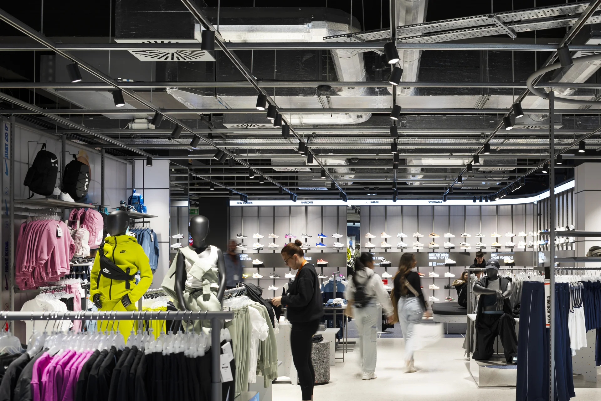 Interior of a Nike store at Trinity Leeds. Features sportswear displays, industrial ceilings, and shoppers browsing apparel.