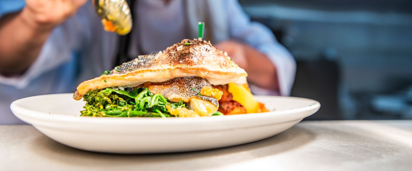 A chef drizzling sauce over a fish dish
