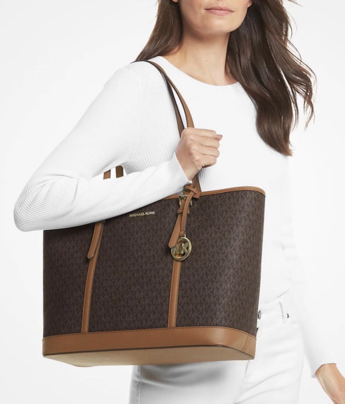 A woman wearing white holding a brown handbag from Michael Kors.
