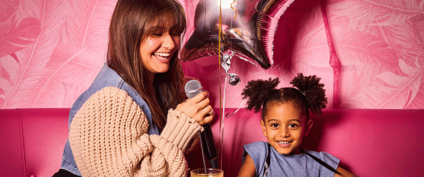 A woman holding a microphone next to a little girl in a karaoke booth