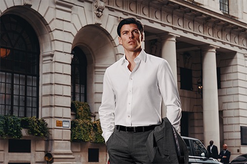 A man in a white shirt stands in a street with his hands in his pockets