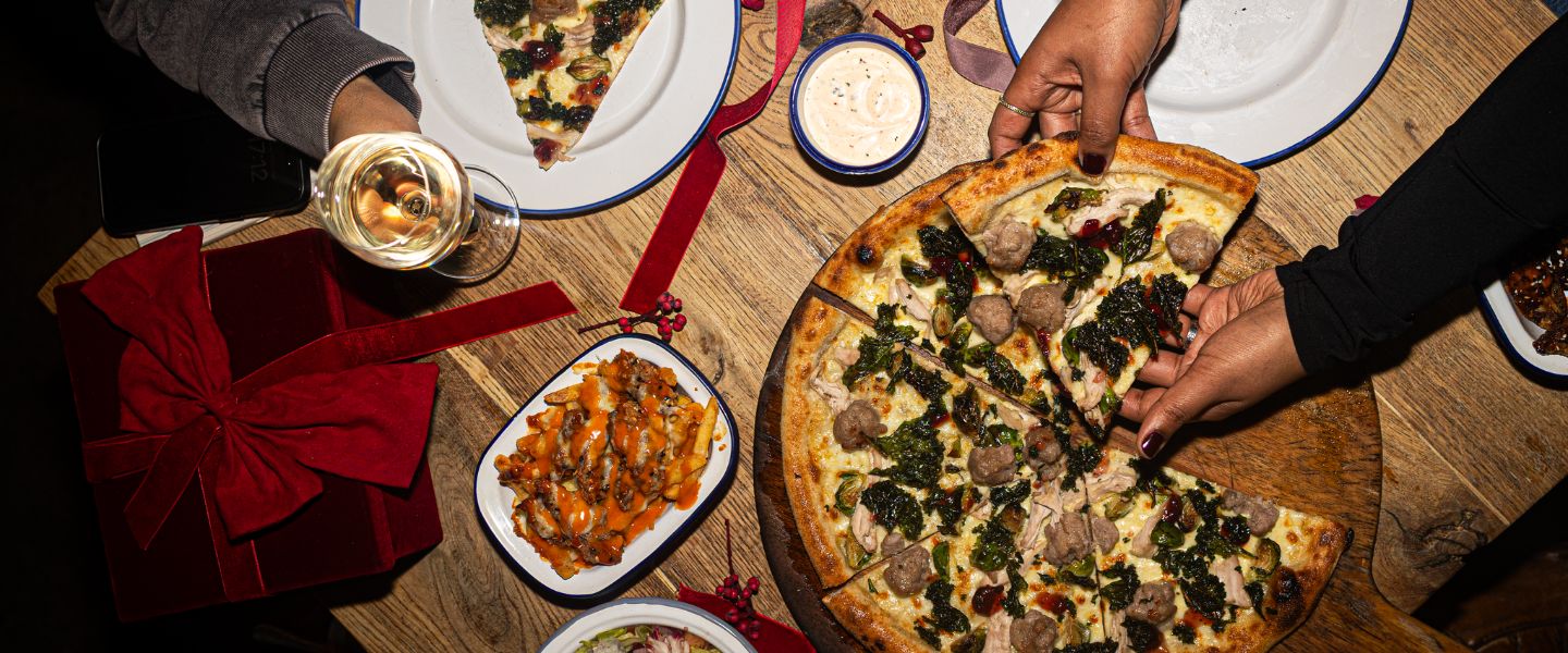 Hands reaching for the Festive Pizza at Street Pizza