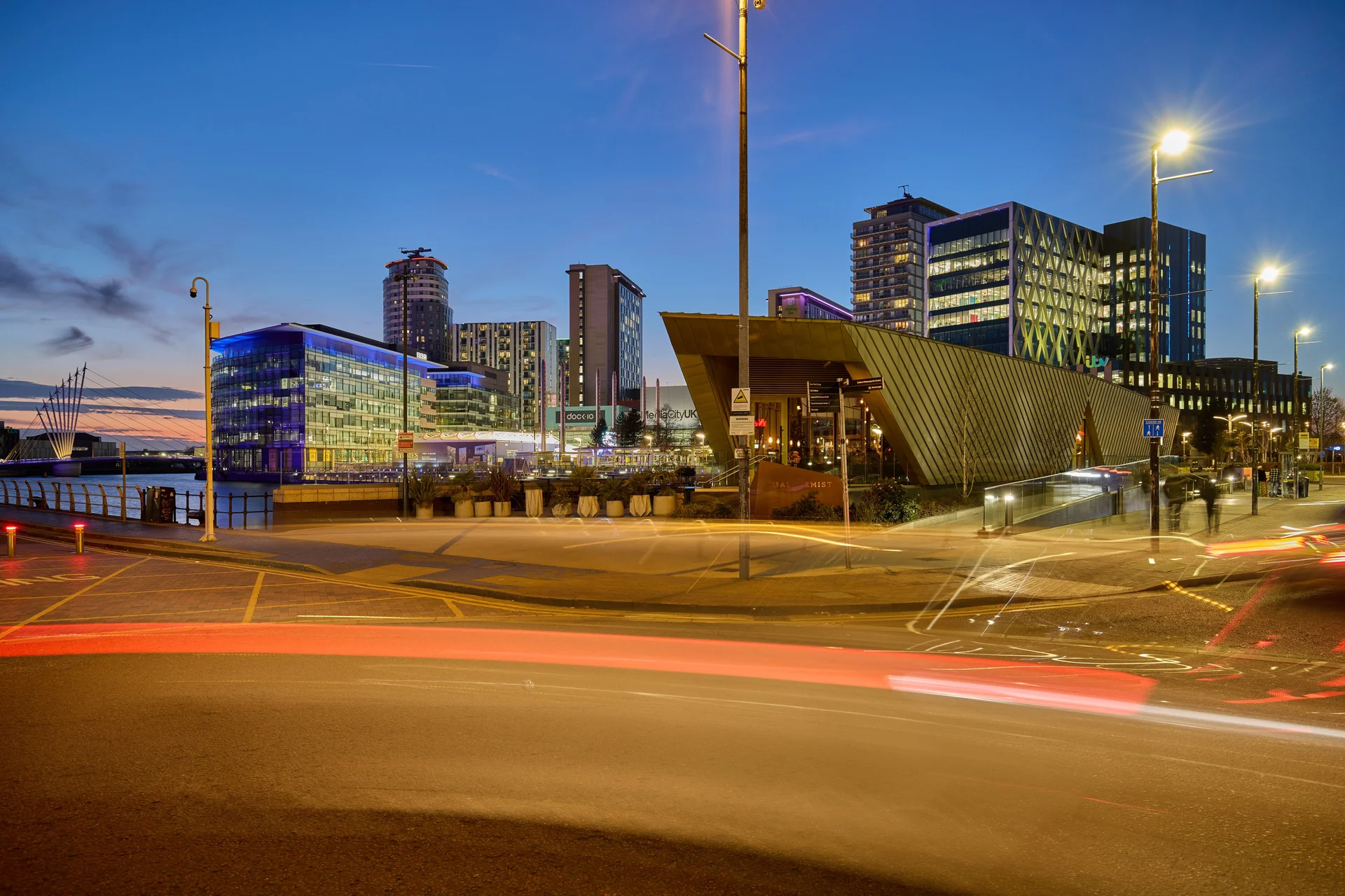Long-exposure shot of the MediaCityUK skyline at twilight, with car light trails on the road and illuminated buildings.