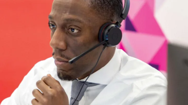 Person in white shirt and tie wearing a headset with a colorful geometric background.