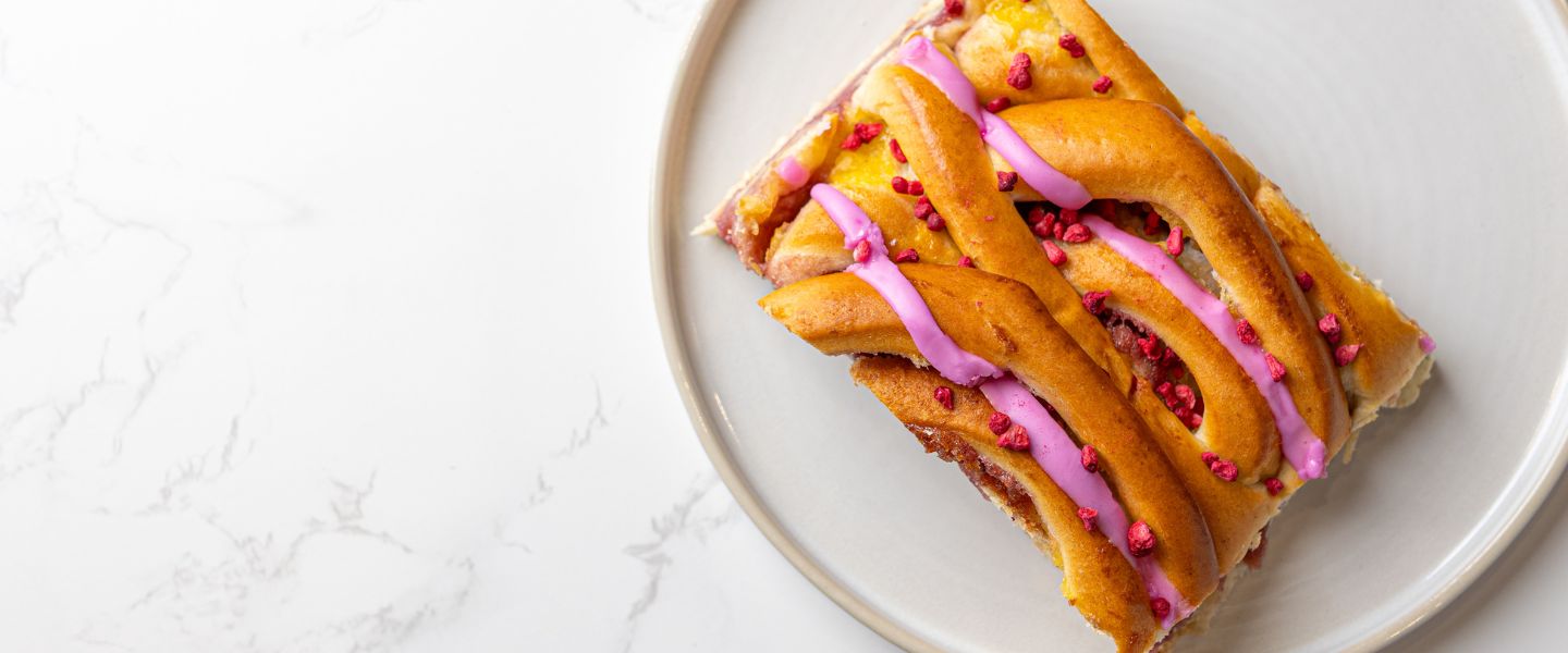 A braided pastry with pink raspberry drizzle.