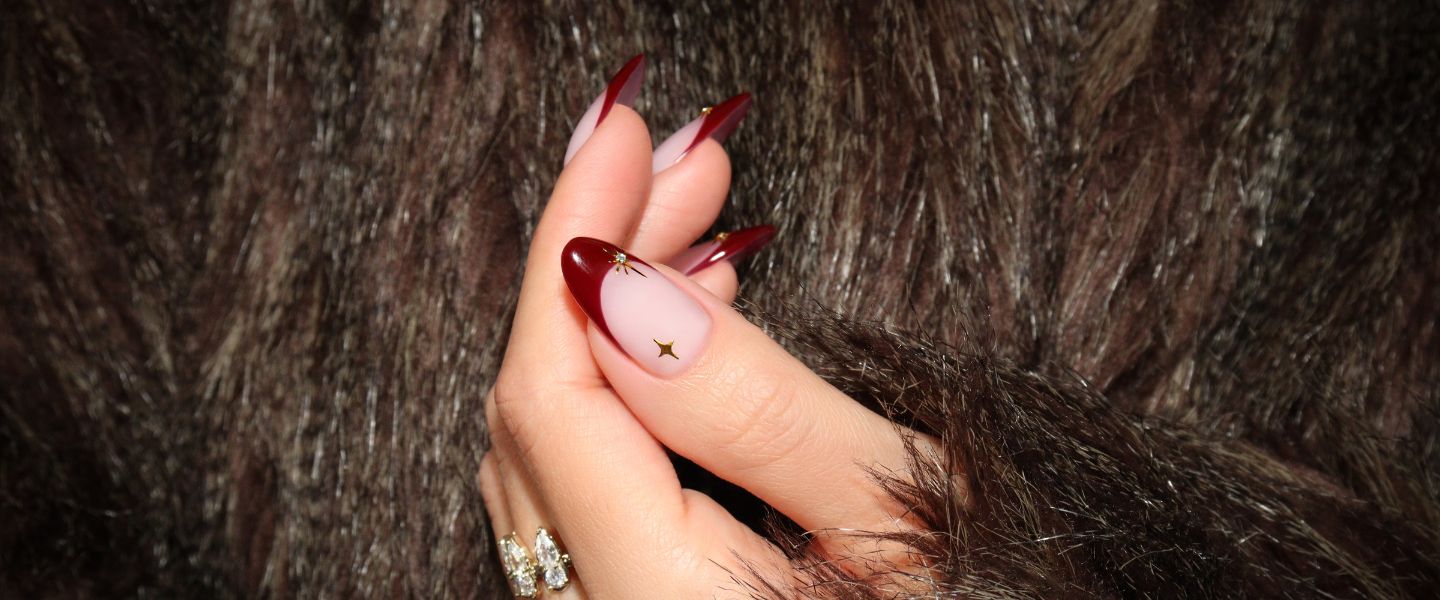 A hand with a burgundy French manicure against a brown fur coat