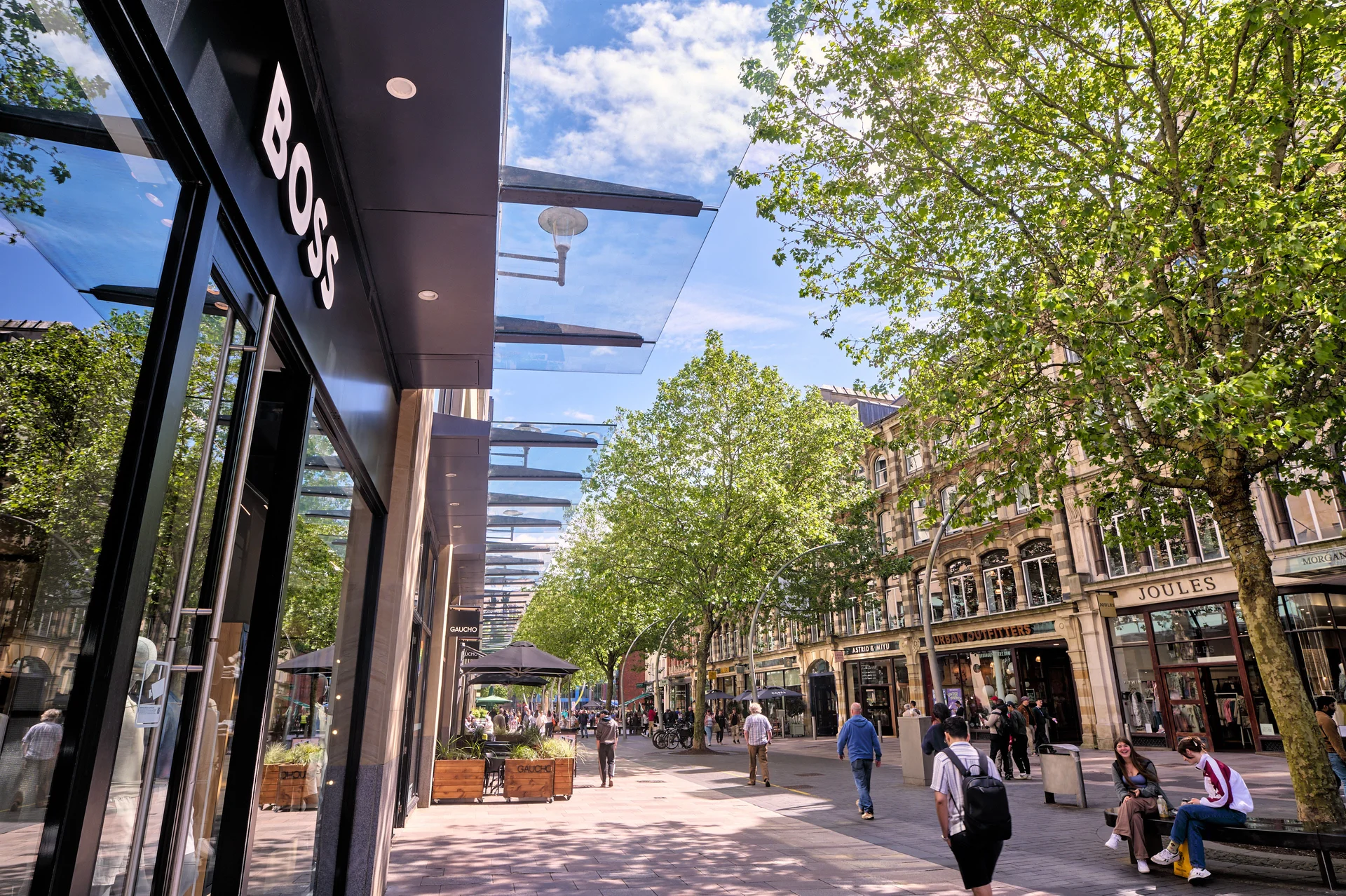 Outdoor urban shopping experience on a sunny day with pedestrians, retail storefronts, and cafe seating.