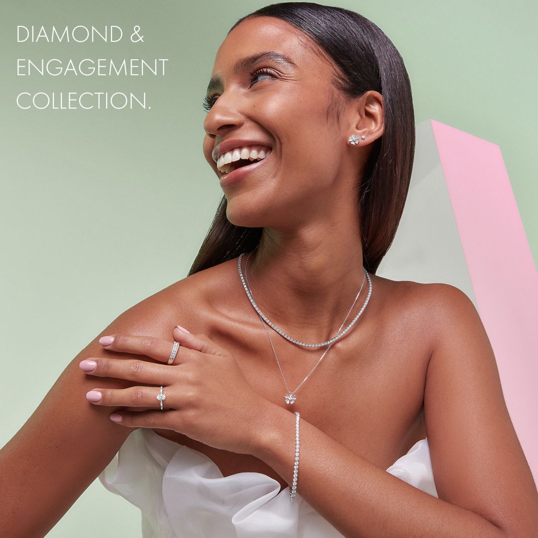 A woman in a white Bardot dress with bare chest and arms, smiling and showcasing a selections of jewellery 