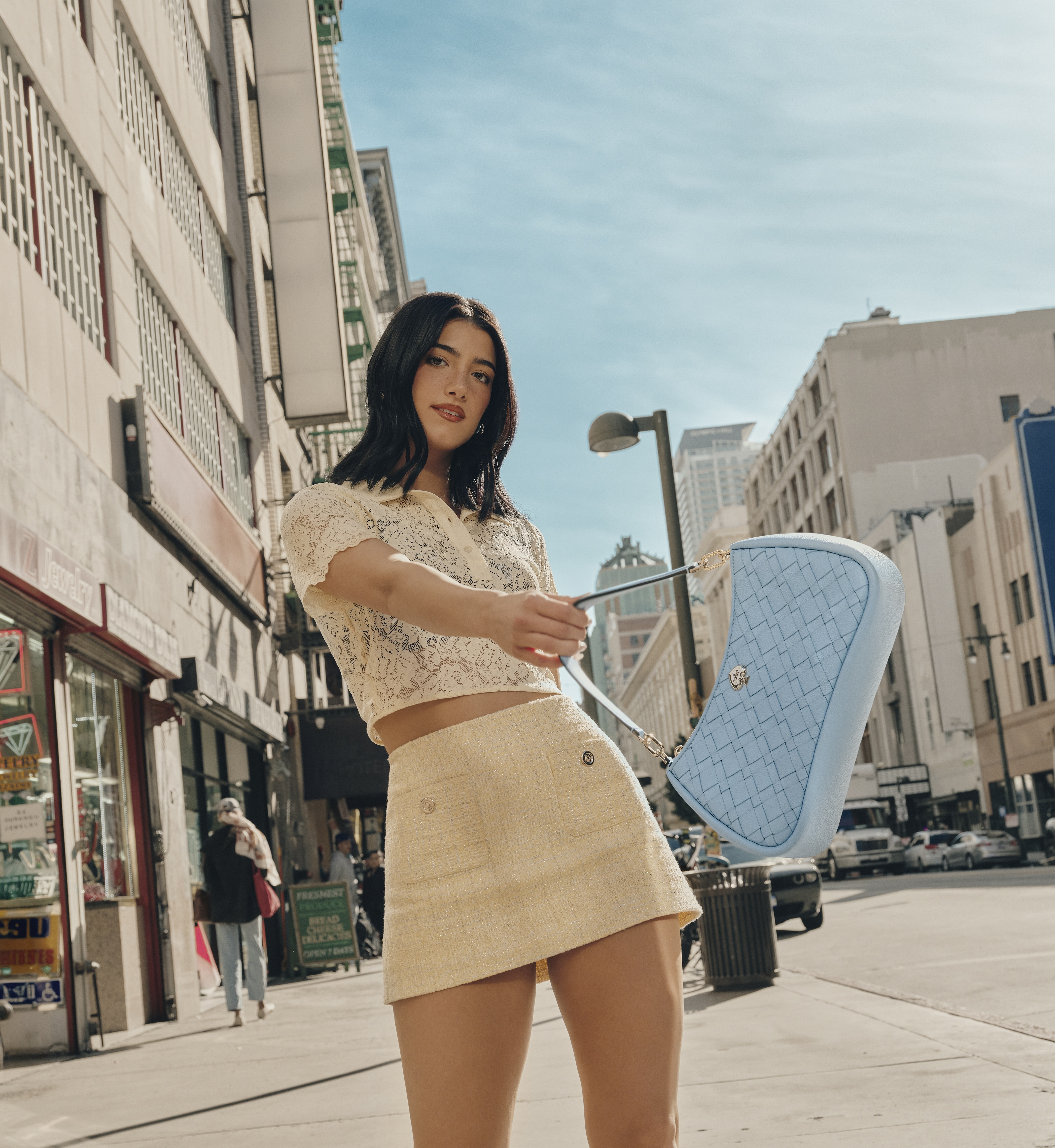 A person holding a new Kate Spade New York handbag with buildings behind