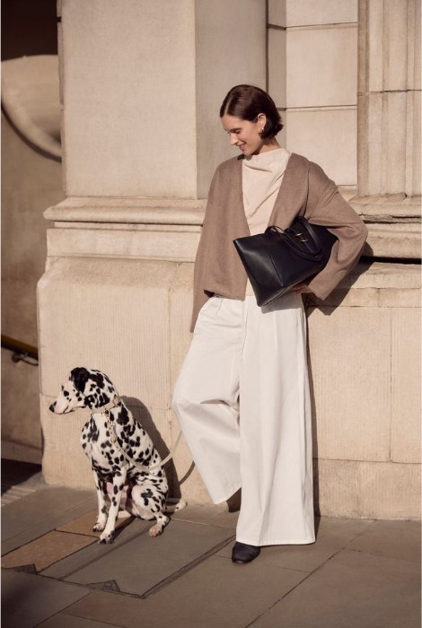 A woman leans against a stone building next to a Dalmatian 