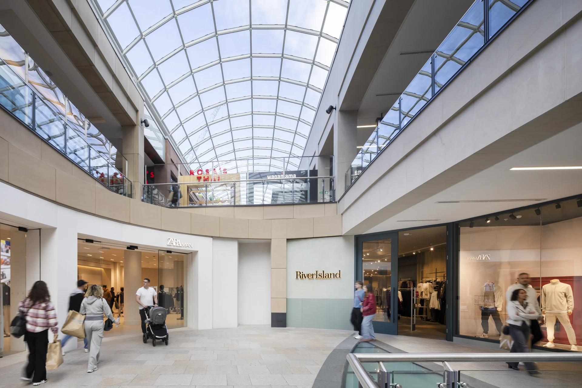 Modern architecture at Trinity Leeds. Shows entrances to Zara and River Island under a soaring glass atrium.