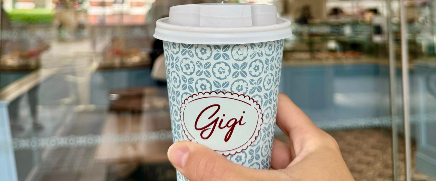 A hand holding a blue takeaway Maison Gigi coffee cup