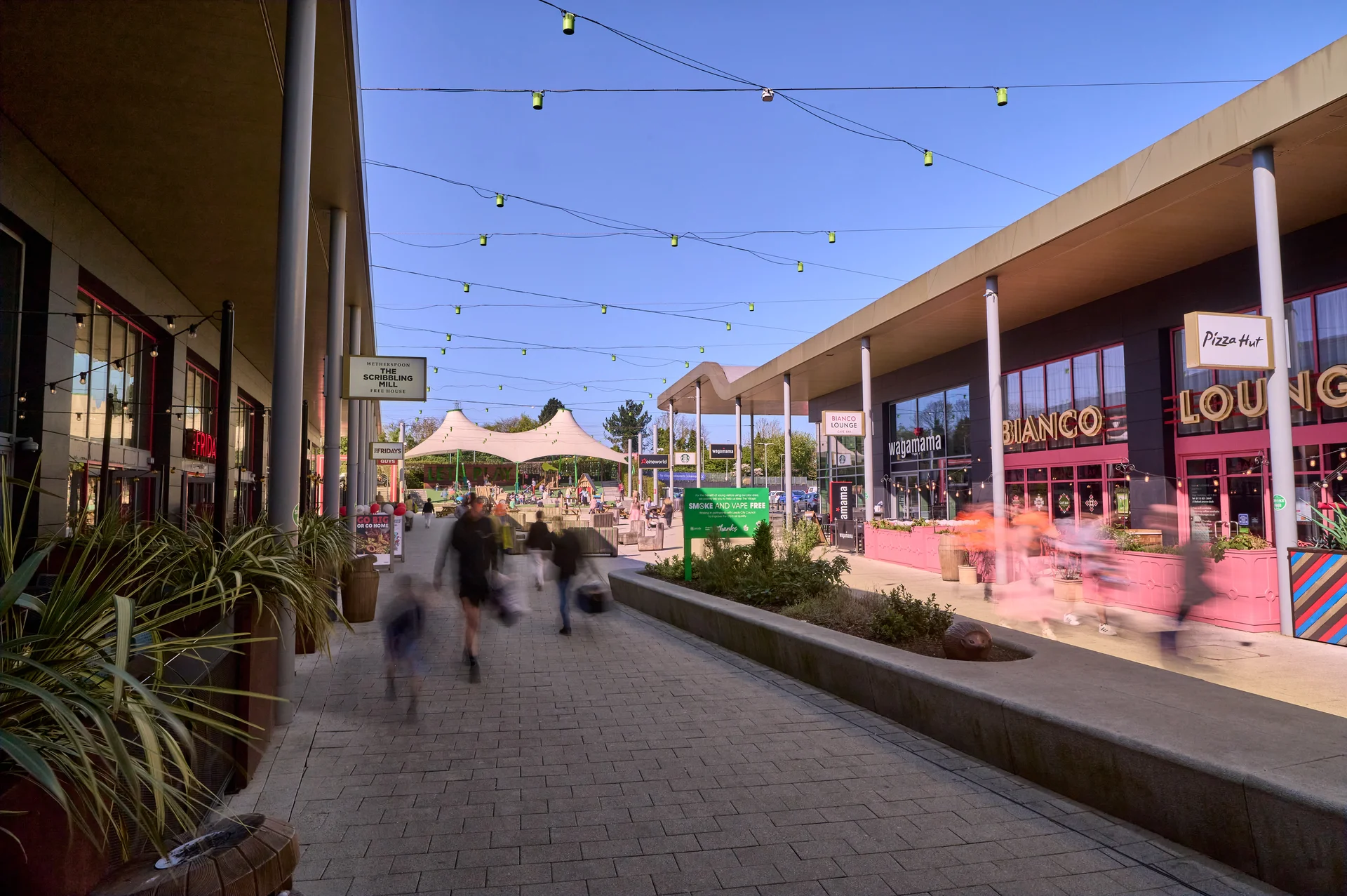 Exterior view of the **White Rose Shopping Centre** outdoor dining and leisure area on a sunny day, featuring covered pedestrian walkways, string lights, and restaurant fronts like **Pizza Hut** and **Loungers**.