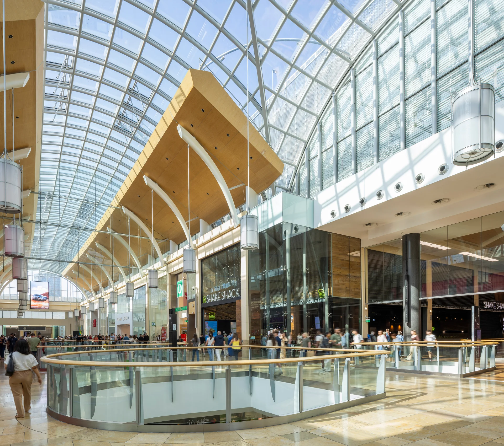 The bright and spacious interior of St. David’s Dewi Sant shopping centre in Cardiff, with shoppers under the large, arched glass roof.