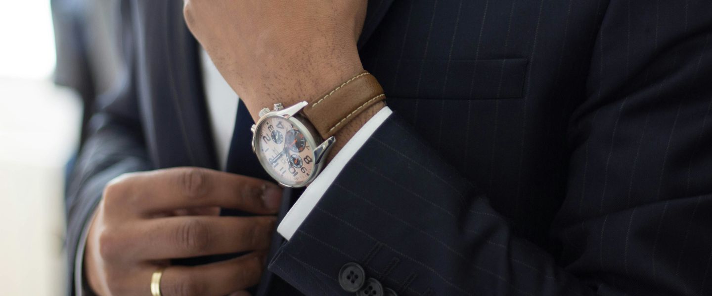 A man wearing a dark suit adjusting his sleeve with a watch on display