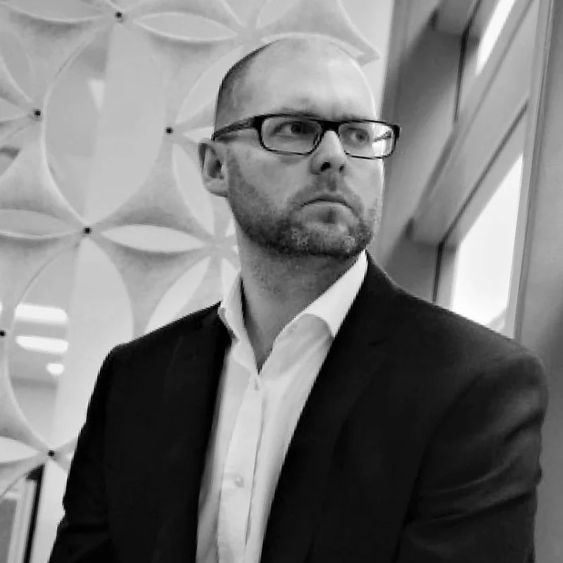 A professional black and white portrait of David Wickens, Group Treasurer at Landsec. He is wearing glasses and a suit, looking off-camera with a serious expression.