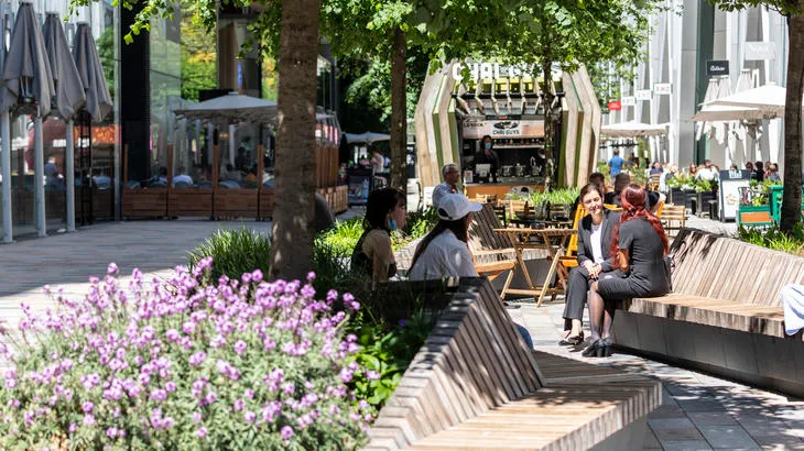 People relaxing on benches in an urban park with a food stall.