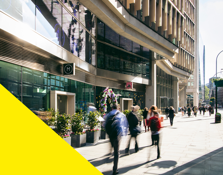 A blurred image of people walking down the street with a yellow triangle in the bottom left corner