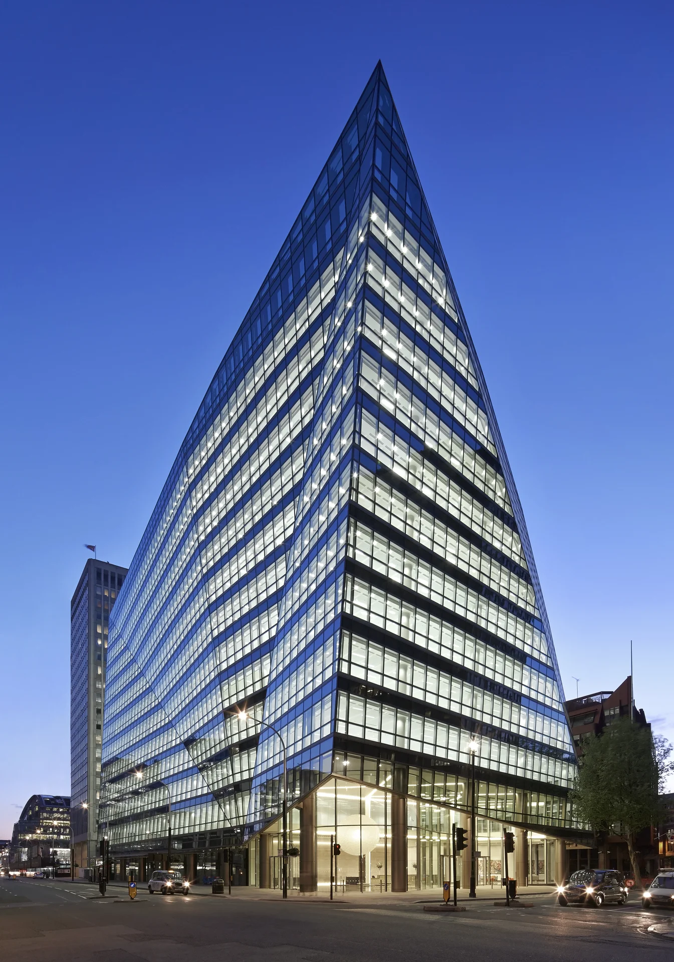 Modern glass office building with sharp, triangular architecture at dusk