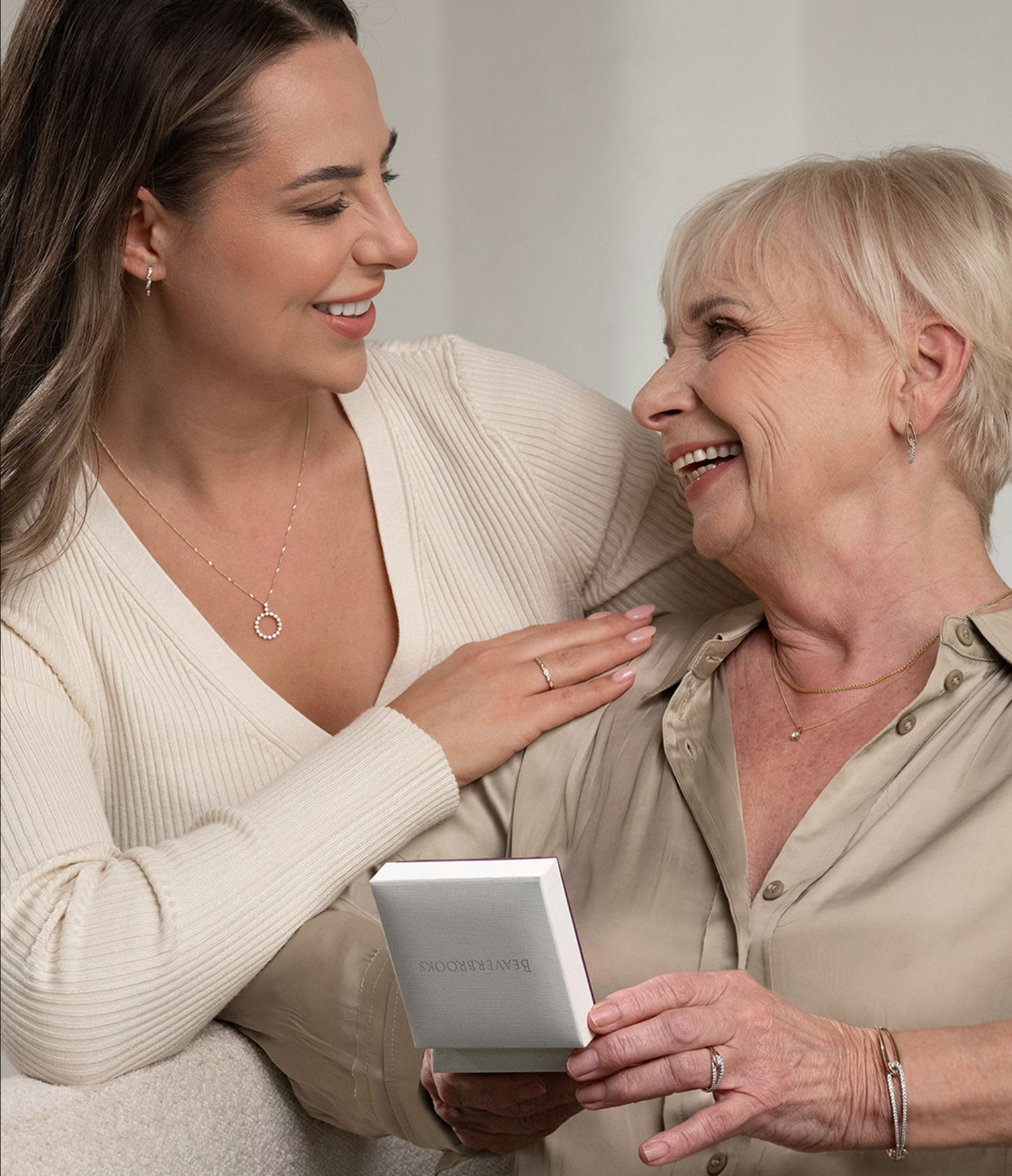 A young woman smiles and holds the shoulder of an older woman holding an open Beaverbrooks jewellery box.