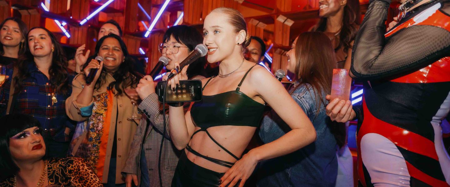 A girl holding a microphone singing karaoke in front of a crowd