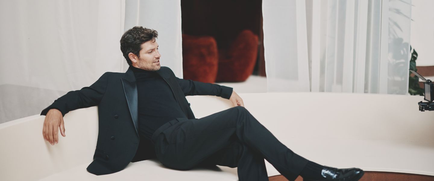A man wearing a black velvet suit on a white couch from Moss