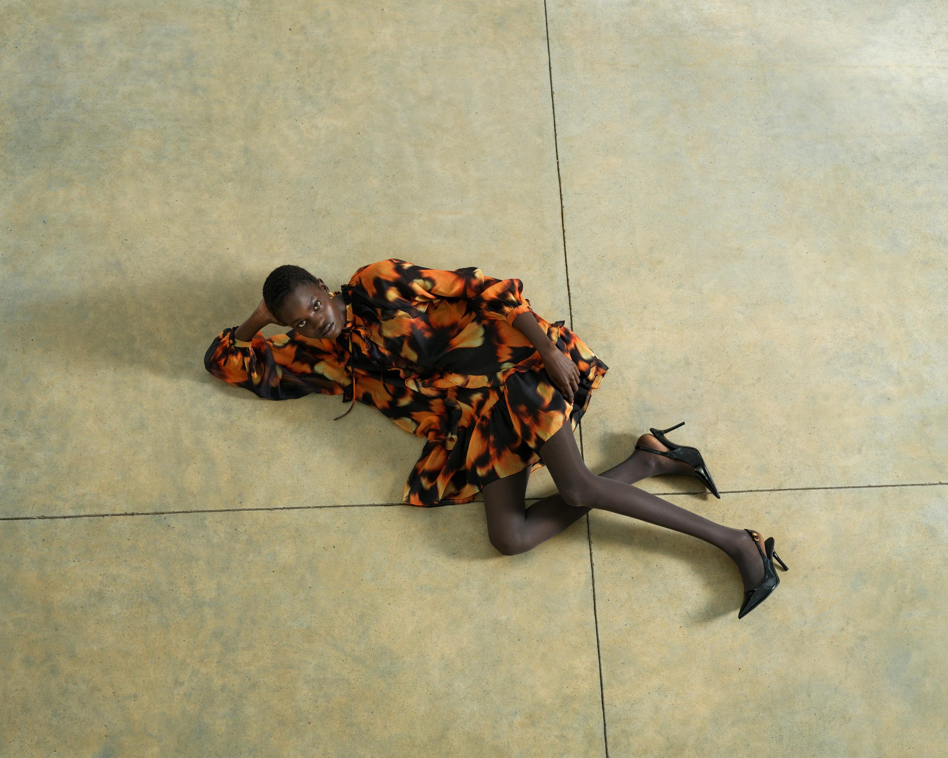 A woman in an orange, patterned dress lying on a stone floor