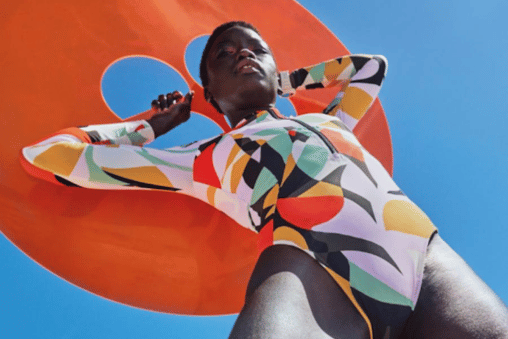 A model wearing a colourful patterned swimsuit and holding an orange inflatable for Sweaty Betty