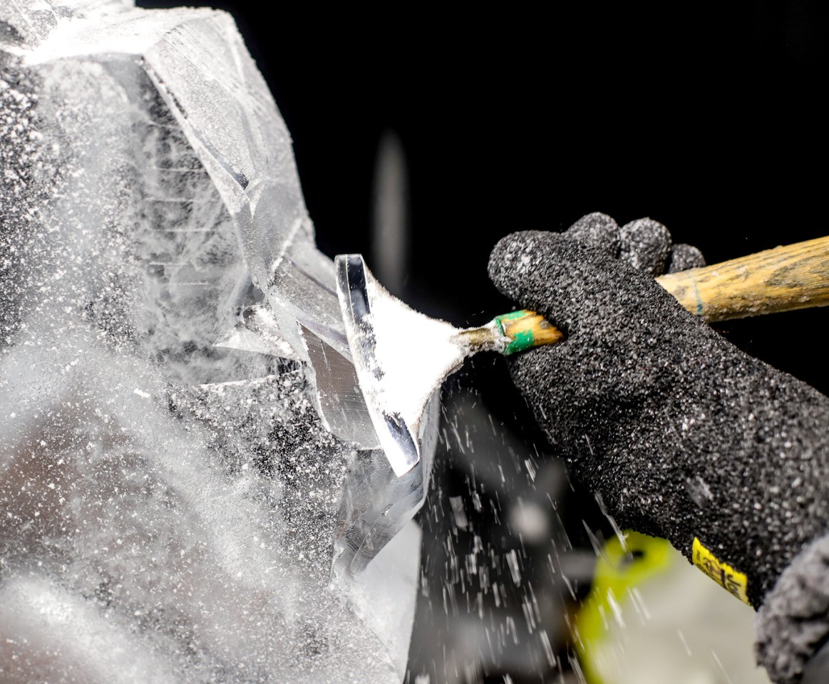Hands in black gloves chisel a block of ice.
