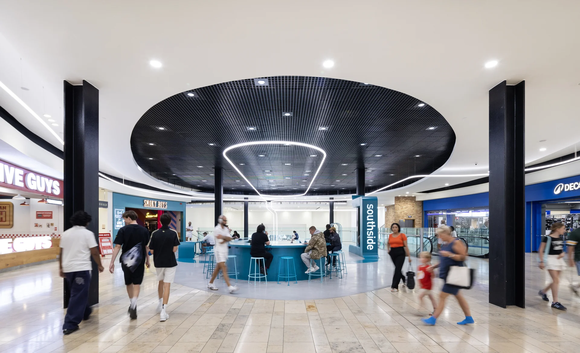 Interior of **Southside Shopping Centre** mall, featuring a modern central seating area with blue stools under a circular black ceiling and bright ring light, surrounded by retail stores.