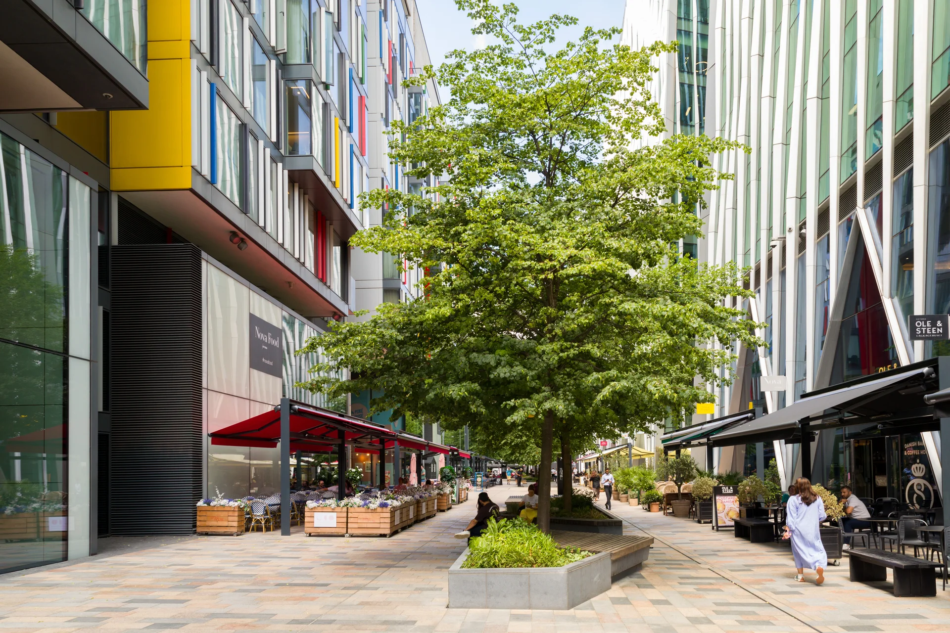 Tree-lined pedestrian plaza with outdoor restaurants and benches in Nova Victoria