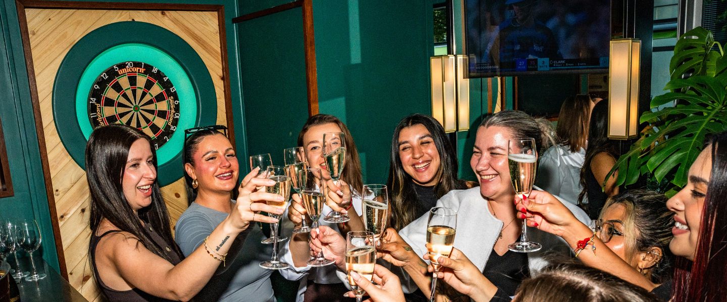 A group of women toasting in front of a dart board