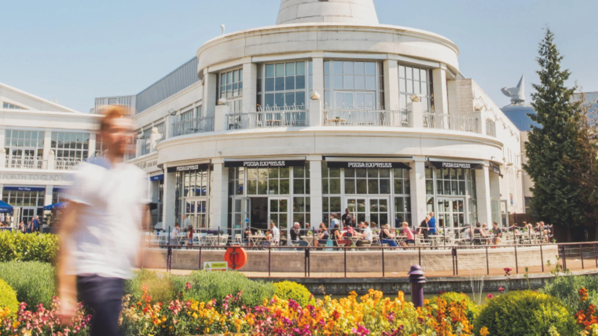 Restaurant with people dining outdoors, flowers in front.