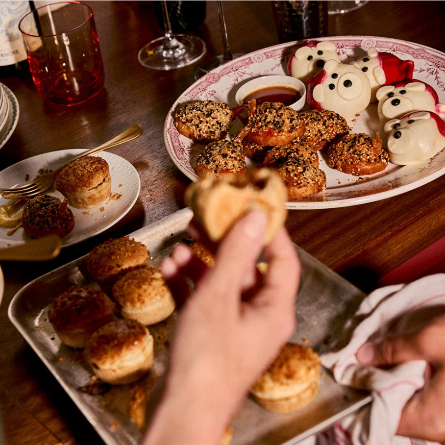 A hand holding a mince pie in front of a table filled with Christmas snacks