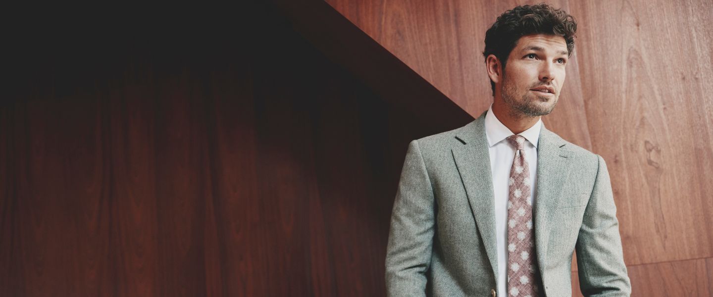 A man wearing a grey suit against a wooden backdrop