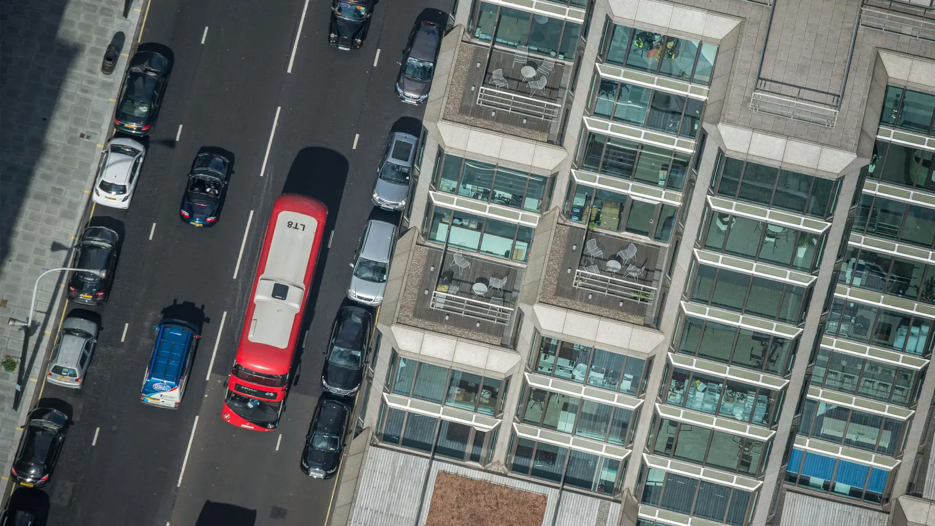 Aerial view of a busy city street with a red double-decker bus and modern building.