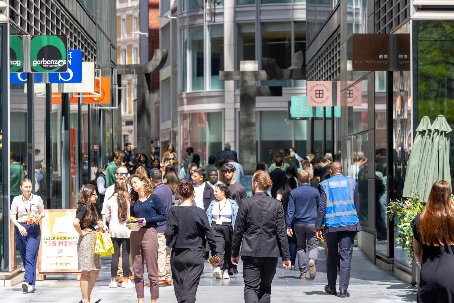 Pedestrian retail street with shops, glass facades, and crowds of people in business attire