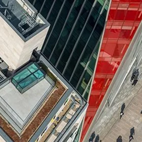 Aerial view showing the juxtaposition of different architectural facades: a **rooftop green space/terrace**, dark vertical glass cladding, and a bright red structural element.