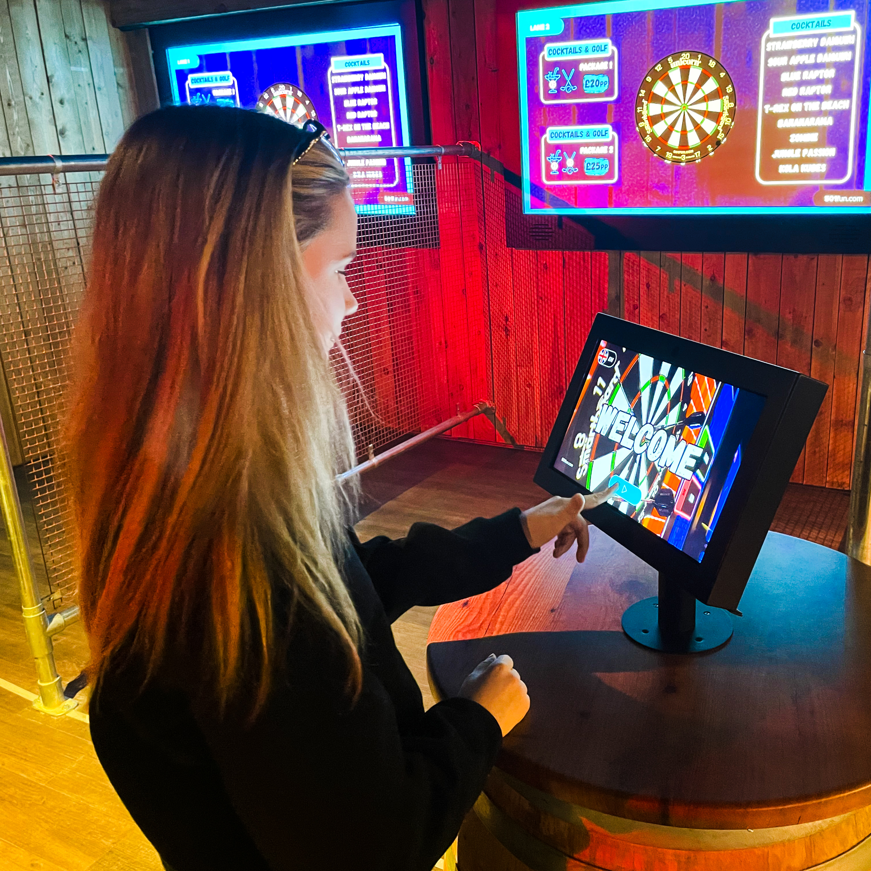 A girl with blond hair and a black jumper playing digital darts on a screen at Volcano Falls shot taken from behind