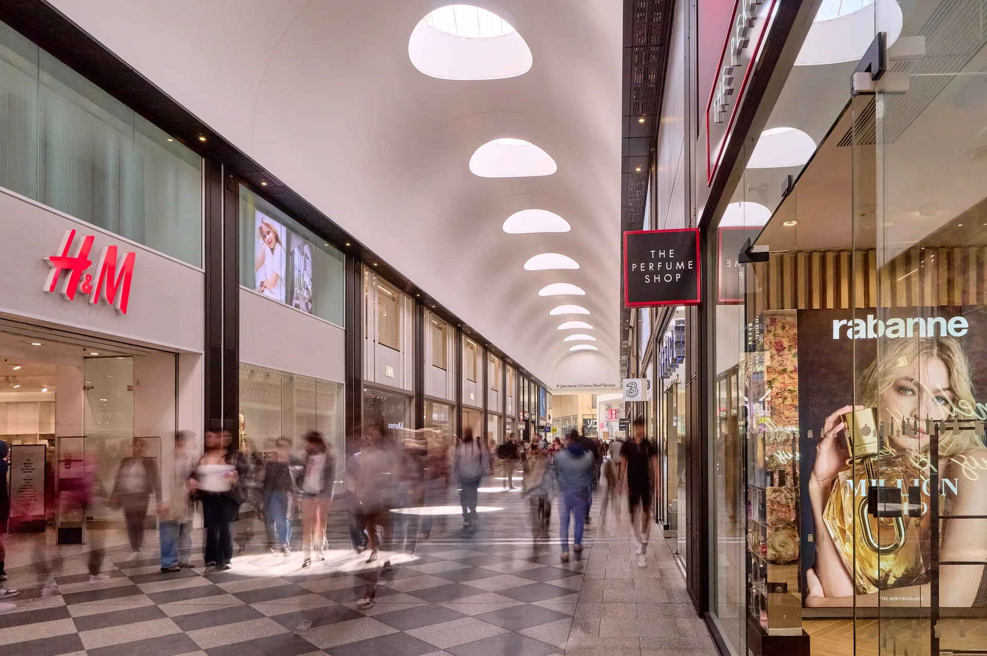 Bright Westgate Oxford walkway with H&M, The Perfume Shop. Modern architecture features distinctive skylight domes.