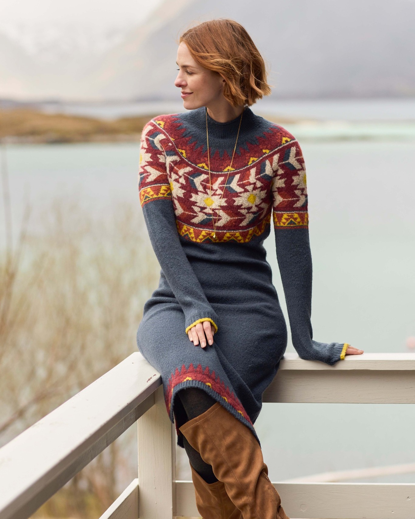 A woman in a patterned woolen dress sits on a balcony by the sea