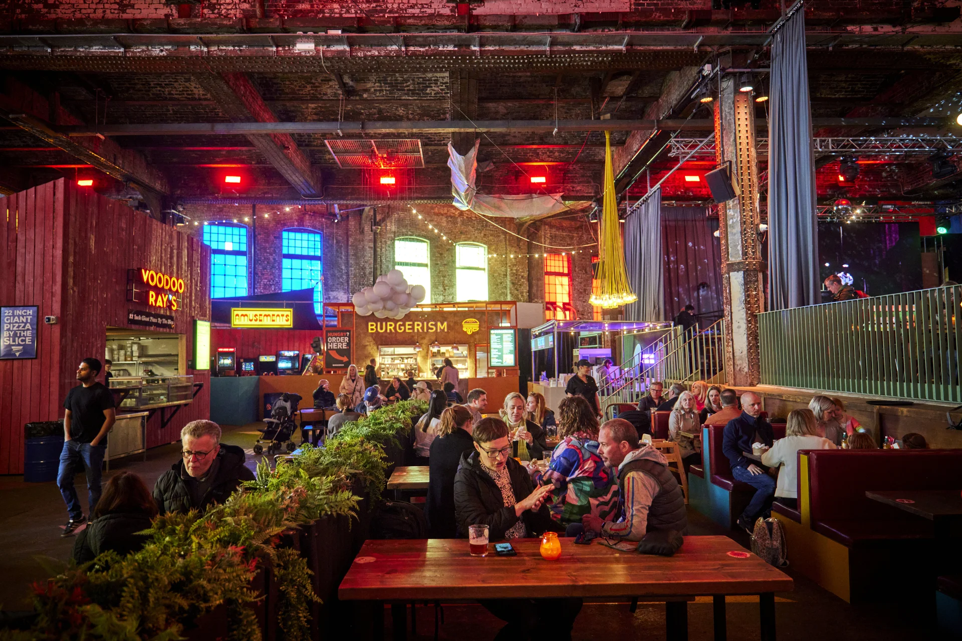 Indoor food hall with vibrant lights, food stalls, and groups dining together.