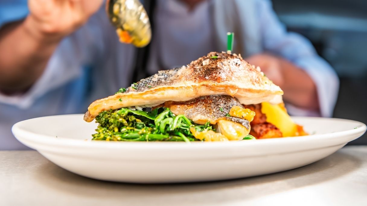 A chef drizzling sauce over a fish dish