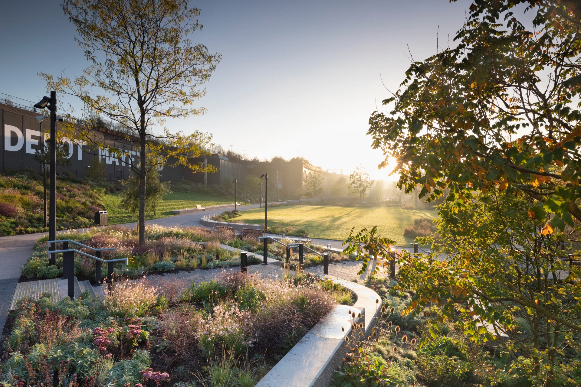 A serene park with winding paths, lush greenery, and benches, bathed in the warm light of a setting sun.
