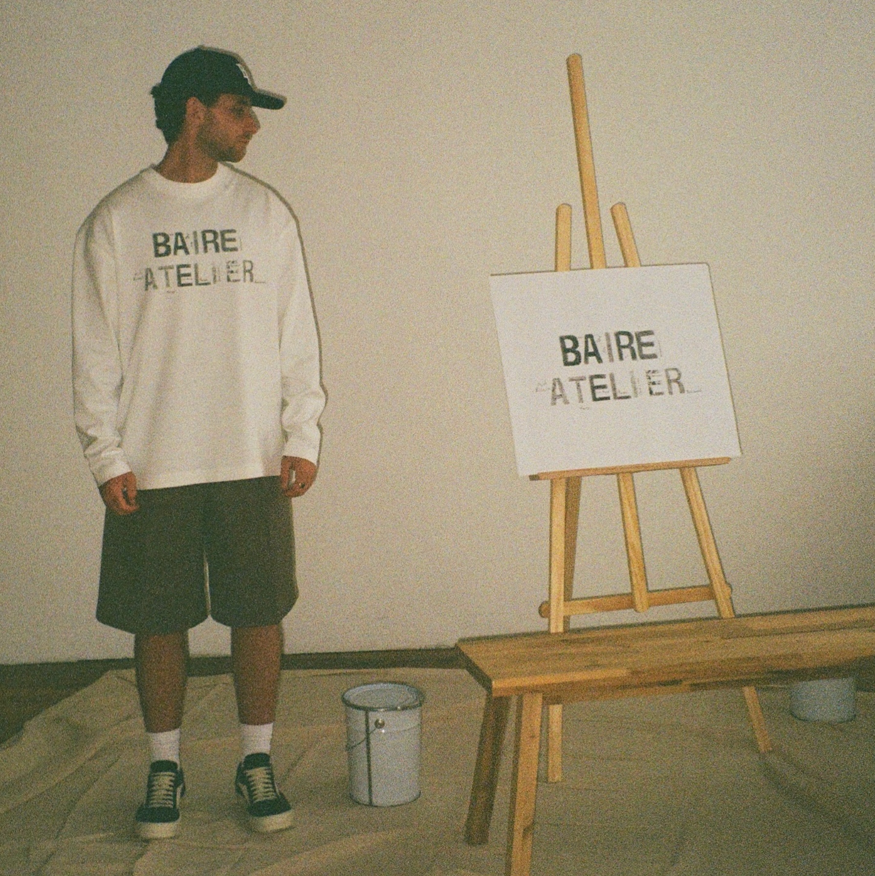 A man wearing a white Baire jumper looking at an easel displaying the text “Baire Atelier.”